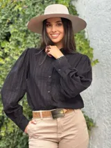 Camisa de manga larga color negro, con cuello alto y cierre frontal de botones. Presenta detalles de encaje y bordados verticales a lo largo de toda la prenda, incluyendo los puños.