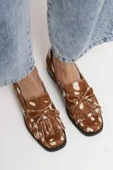 Mocasín de cuero con estampado animal print tipo vaca, de horma cuadrada. Presenta detalle de flecos y lazo decorativo en el empeine, con taco bajo cuadrado.