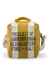 Bolso tipo baúl color amarillo mostaza, confeccionado en cuero con estampado de texto en negro. Tiene doble asa de mano de cinta de algodón blanca con refuerzo de cuero, correa bandolera extraíble de cordón blanco, cierre superior con cremallera de doble cursor y bolsillos internos.