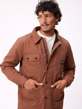 Sobrecamisa de algodón color marrón, con cierre frontal de cremallera y botones a presión. Presenta cuello clásico, dos bolsillos frontales con solapa y cierre de botón, y forro interior de poliéster.