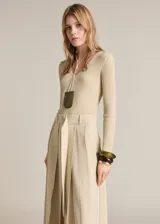 Vestido midi de diseño combinado con cuerpo de punto de canalé en color beige y falda de tablas en el mismo tono. Presenta cuello en pico, manga larga y cinturón desmontable con hebilla metálica.