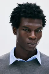 Buzo de punto fino color gris oscuro, de manga larga y cuello redondo, con remates acanalados en cuello, puños y bajo.