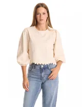 Blusa color beige con bordado floral al tono en el pecho y la espalda. Presenta mangas largas abullonadas con frunces en los hombros y puños festoneados. El ruedo cuenta con un acabado festoneado en ondas y la espalda incluye una abertura tipo gota con cierre de botón.