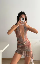 Vestido corto de microtul con estampado abstracto en tonos marrones y beige. Diseño con escote halter profundo, espalda descubierta, detalle de frunce con aplique de estrella de mar dorada en la cintura y falda con volados y terminación irregular. Incluye short de forro.