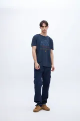 Remera de algodón color azul marino con cuello redondo y mangas cortas. Presenta un estampado gráfico central con texto en tonos azul claro, rojo y amarillo, incluyendo una pequeña estrella.