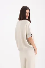 Sweater de punto color beige, con cuello redondo, mangas cortas con dobladillo y detalle de botón lateral, y terminaciones en lurex.