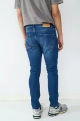 Jean de corte slim fit en color azul oscuro, con diseño clásico de cinco bolsillos, cierre frontal con botón y cremallera.