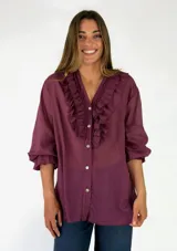 Blusa bordó de seda de manga larga con volados en el frente y botones visibles.
