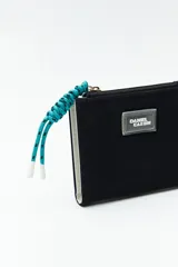 Billetera compacta de símil cuero color celeste claro, con cierre superior y un tirador de cordón trenzado multicolor. Posee un parche frontal con el logo de la marca.