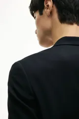 Blazer negro de corte slim fit, con solapas de muesca finas, ojal decorativo, botonadura sencilla, bolsillo superior insertado, bolsillos delanteros con solapa, dos bolsillos interiores, botones decorativos en los puños y abertura doble atrás.