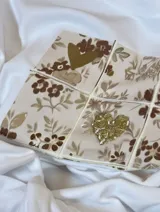 Remera de manga larga color blanco, con cuello redondo y corte recto. Presenta un estampado frontal rectangular dividido en cuadrículas con motivos florales y un corazón central en tonos dorados.