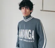 Campera tejida de algodón en color rojo, con cierre frontal completo, cuello alto y puños acanalados con detalles de rayas blancas. Presenta un diseño gráfico con texto blanco en el frente.