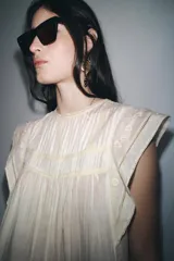 Blusa blanca sin mangas confeccionada en hilatura con viscosa y algodón. Tiene cuello redondo, detalle de bordados a contraste y cierre en espalda con abertura y botón.