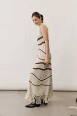 Vestido largo de punto con diseño geométrico y de ondas en color negro y crudo, sin mangas, con escote halter y detalle de flecos en el ruedo.