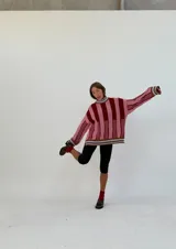 Buzo oversize de punto con cuello alto, mangas largas y diseño a rayas verticales en tonos rosa y bordó.