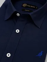 Camisa de algodón color celeste, corte slim fit, con cuello clásico, botones blancos con costura azul y un bordado de un pájaro en el pecho.
