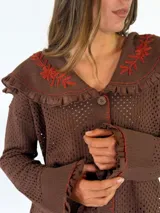 Saco tejido de punto color azul con diseño calado, cuello grande con bordados florales en tono crudo, volados decorativos y cierre frontal con un botón.