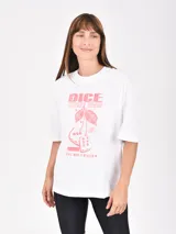 Remera blanca de corte oversize con cuello redondo y mangas cortas. Presenta un estampado frontal en color rosado con diseño de dados y cerezas, acompañado de texto decorativo.