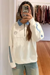 Buzo oversized de algodón color blanco, con cuello tipo camisa en denim celeste, medio cierre frontal, logo bordado y tiras decorativas en las mangas.