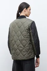 Campera bomber reversible con diseño capitoneado, cuerpo en color verde oliva y mangas negras. Presenta cierre frontal, cuello, puños y ruedo acanalados, y un bolsillo de parche en color beige.