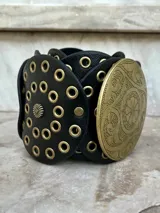 Cinto faja de cuero sintético negro con hebilla metálica dorada con diseño circular calado.