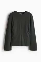 Top de manga larga confeccionado en punto de algodón, con cuello redondo, hombros caídos y detalle de frunces laterales que generan un bajo acampanado.