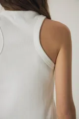 Musculosa de morley color blanco, con escote estilo halter y detalle de texto bordado en negro en el pecho.