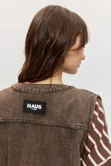 Chaleco de denim marrón con efecto acid wash, cierre frontal con botones metálicos y bolsillos appliquè en el frente.