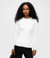 Blusa peplum de manga larga en punto roma color blanco, con cuello redondo y diseño estructurado de corte amplio en el ruedo.