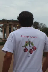 Remera de algodón con efecto acid wash en color azul, corte recto, mangas cortas y estampa en la espalda con diseño pixelado de cerezas y el texto "Cherry Season".