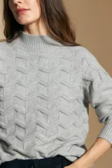 Sweater de punto color beige con diseño geométrico en relieve, cuello alto y mangas largas con puños acanalados.