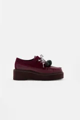 Zapato tipo mocasín de plataforma color bordó, confeccionado en una combinación de cuero liso y gamuza. Presenta cordones bicolores con detalle de borlas decorativas en el empeine.