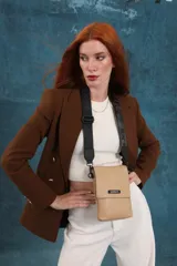 Phonebag pequeña color mostaza, confeccionada en cuero sintético, con solapa frontal y correa ajustable con logo de la marca.