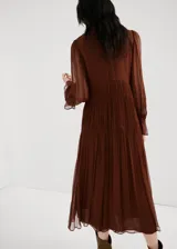 Vestido midi marrón de viscosa transparente, con diseño plisado, cuello alto fruncido y mangas largas abullonadas con puños elásticos. Presenta detalles de costuras fruncidas en la cintura y falda escalonada con vuelo.