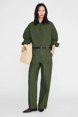 Chaqueta Yuma de inspiración utilitaria, color verde militar, confeccionada en algodón estructurado con acabado suave y desgastado. Presenta una silueta relajada, bolsillos de parche frontales y cierre de botonadura central con botones en tono gris plomo.