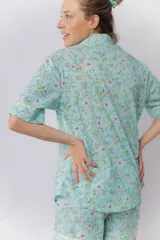 Pijama de algodón estampado con flores en tonos pastel sobre fondo verde menta. Incluye una camisa de manga corta abotonada con cuello solapa y un short con elástico en la cintura, ambos con detalles de picot en los bordes.