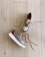 Championes de cuero color visón con cordones marrones, suela blanca y base color caramelo.