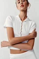 Top de punto rib color blanco, con cuello solapa, manga corta y cierre frontal con botones dorados.