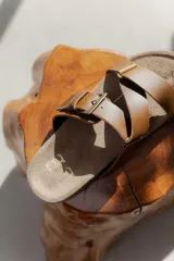 Sandalias bajas de cuero color beige con doble tira de cuero negro con textura y hebilla metálica.
