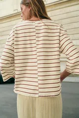 Camiseta de algodón a rayas horizontales en tonos marrones y beige, de corte regular fit, cuello redondo a contraste de color marrón oscuro y mangas largas por debajo del codo. Presenta diseño de bajo asimétrico.