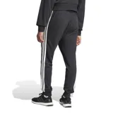 Pantalón de jogging Adidas modelo M 3s Ft Tc Pt, color negro con las tres tiras características en los laterales de color blanco y el logo de la marca bordado en la pierna izquierda. Cuenta con cintura elástica con cordón de ajuste y puños en los tobillos.