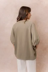 Buzo oversize color beige, con escote redondo, mangas cortas amplias de corte raglán y terminación frontal asimétrica en punta con aberturas laterales.