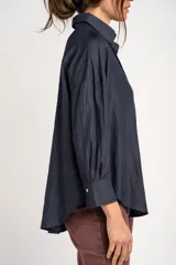 Camisa azul marino de corte oversize, con cuello clásico, cierre frontal con botones, mangas largas con puños anchos y un bolsillo aplicado en el pecho.