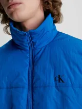 Chaleco acolchado azul eléctrico con cierre frontal, cuello alto y logo de Calvin Klein en el pecho.