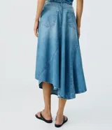 Pollera midi de jean color azul, con cintura baja, diseño asimétrico y ruedo irregular.