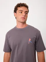 Remera de manga corta color amarillo, corte holgado, con gran estampado en la espalda de un perro en bicicleta con una tabla de surf y un loro, acompañado del texto "Wild by Nature Rusty Worldwide".