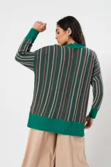 Sweater verde esmeralda de cuello redondo y manga larga, con terminación acanalada en puños y ruedo. Presenta tajos laterales y diseño de rayas verticales en tonos blanco y rosa.