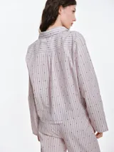 Camisa de dormir de popelina de algodón, con estampado de rayas verticales y pequeños motivos geométricos. Presenta cuello camisero, mangas largas y cierre frontal mediante lazos ajustables.