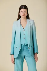 Saco de mujer con solapa tipo chal, corte estructurado y cierre frontal con botón metálico decorativo. Presenta bolsillos con solapa y un diseño elegante en color turquesa.