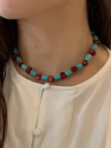 Collar choker hecho a mano con cuentas cilíndricas de turquesa reconstituida y pequeños corales rojos intercalados, con cierre ajustable de acero dorado.